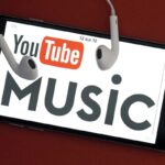 Smartphone com YouTube Music na tela e fones de ouvido sobre ele.