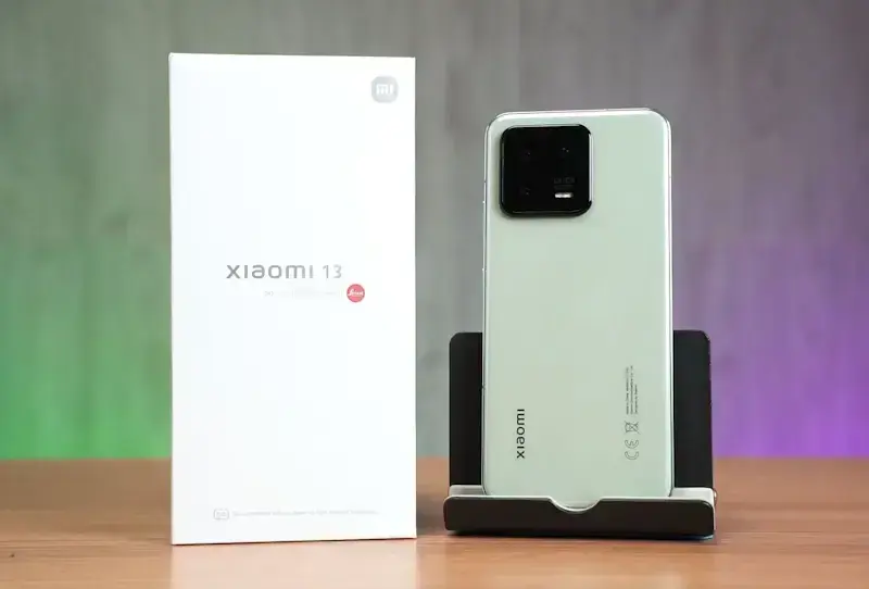 Quais são os melhores smartphones Xiaomi para comprar no momento? Foto ilustrativa do Xiaomi 13 5G, parte traseira posicionado em pé em suporte ao lado de sua caixa.